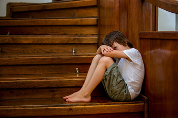 Sad child, sitting on a staircase in a big house, concept for bullying