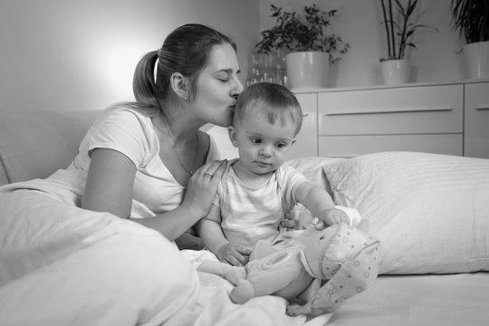 Black and white portrait of young mother kissing her baby son before going to sleep