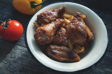 Appetizing chicken pieces and french fries with seasoning in a beautiful old bowl and on an old wooden background, yellow pepper and tomato and a background