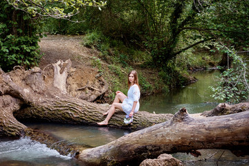 Young pretty woman in a white dress walking and posing in a forest near the river