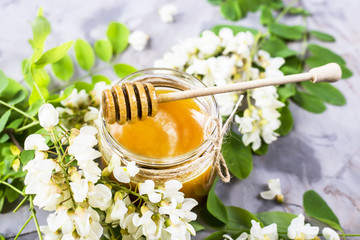 Obraz na płótnie Canvas Honey from acacia and other nectar among the flowering branches of acacia. On a gray background. With a wooden spoon for honey
