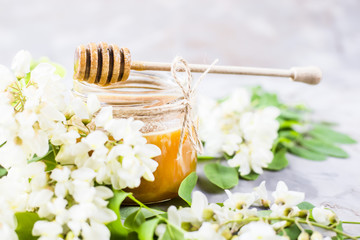 Obraz na płótnie Canvas Honey from acacia and other nectar among the flowering branches of acacia. On a gray background. With a wooden spoon for honey
