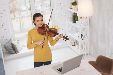 Look at me. Beautiful brunette keeping smile on face while playing the violin