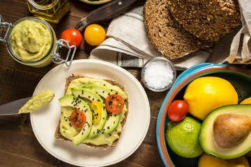 Fresh Avocado Spread Guacamole and Slices with Cherry Tomato and Black Sesame on a Piece of Bread. Healthy Breakfast Concept.
