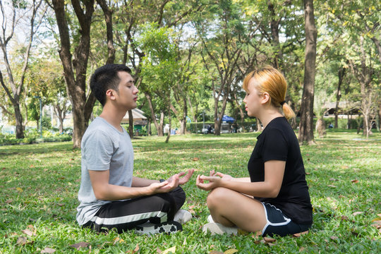 Young love couple making a meditation to calm their mind after exercising in park encircle with a warm light sunshine in afternoon. Yoga Sport and Healthy lifestyle concept. Couple outdoor mind peace.