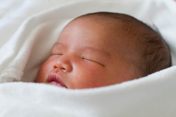 Newborn infant baby girl in white blanket sleeping in bed