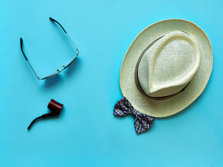 Pipe and glasses lying near straw hat and bow tie on blue background