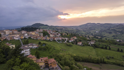 Aerial view of the sun setting behind the mountains. In the valley, nature is a small agricultural town.