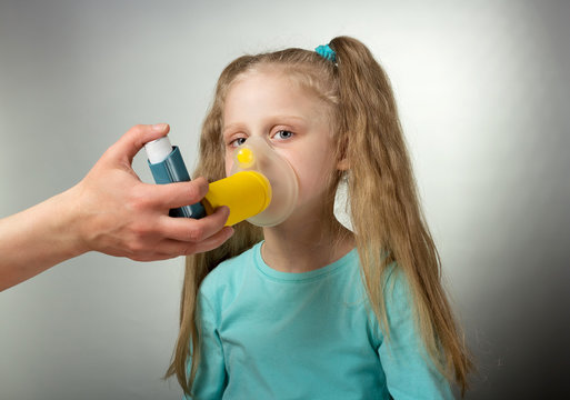 Sick child inhales medicine through mask on gray