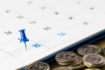 Pin on calendar on  30th of the month with blurred coins, business concept