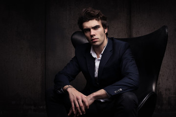 Portrait of a beautiful young man sitting in a chair. Stylish in appearance