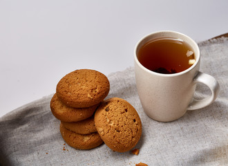 White porcelain mug of tea and sweet cookies on homespun napkin over white background, top view, selective focus