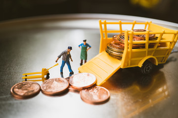 Miniature people, closeup worker lifting stack coins into truck using as business and financial concept