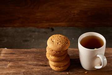 White porcelain mug of tea and sweet cookies on piece of wood over wooden background, top view, selective focus