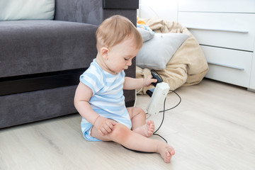 Unattended baby boy sitting on floor and playing with electric cables. Concept of baby in danger