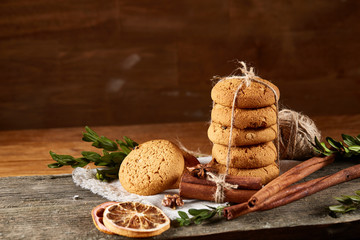 Christmas composition with pile of cookies, cinnamon and dried oranges on light wooden background, close-up.