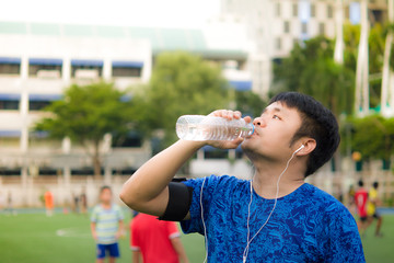 Asian sport man is drinking fresh water in transparent plastic bottle during listening