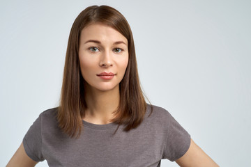 Studio portrait of a young beautiful brunette woman with clean healthy skin with neutral emotions looking at the camera. 