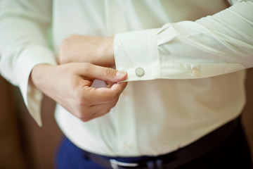 Grooms morning preparation, handsome groom getting dressed and preparing for the wedding, the groom wears cufflinks in a white shirt