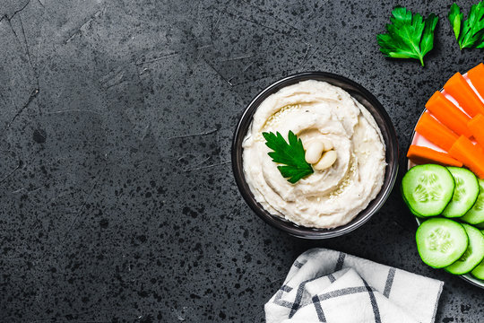 Roasted garlic white bean dip on dark concrete background. Top view, space for text. 