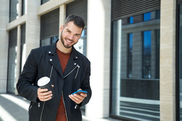 Portrait of handsome man with beard with cheerful positive emotions walking down the street on Sunny day with Cup of coffee
