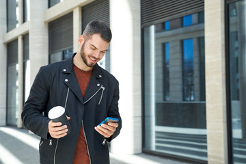 A man in a black jacket with a smile responds to a message on the phone. The concept of mobility, wireless communication