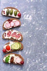 The border is assorted from a variety of bruschetta on a gray background. Bruschetta with sausage and vegetables. Top view, copy space.