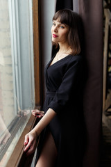 Photo of young brunette in black dress near window