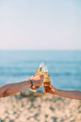 Closeup of hands toasting with bottles of beer at the beach 