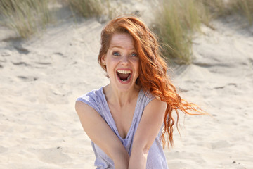 Hübsche rothaarige Frau sitzt an einem Strand und schreit vor Begeisterung