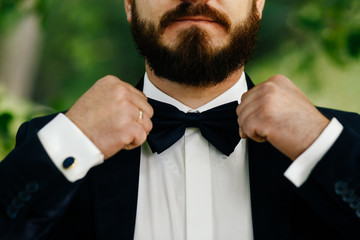 the bridegroom spits a black bow-tie. man with two hands touches a bow-tie
