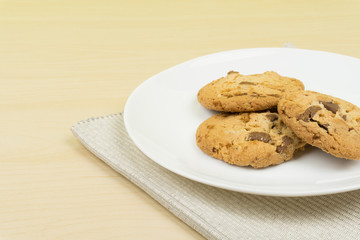 three pieces of chocolate chip cookies in a white round dish on the wooden table.