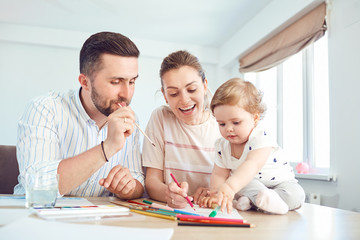Happy family draws paints on a paper at the table in the room.