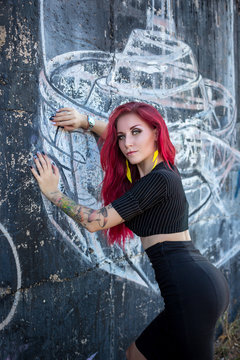 sexy redhair woman in hooligan outfit and sunglasses posing against graffiti wall