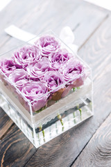 Pastel purple hue roses in clear acrylic crystal flower box. Square glass gift box. On wooden table from above