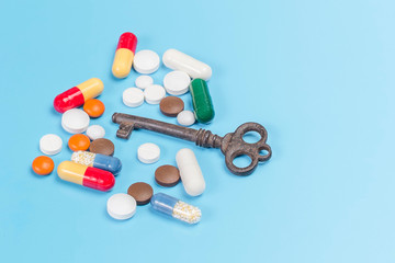 Medications of different colors and shapes with a copper key, on a light blue background