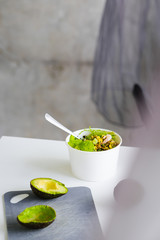 Take away salad in disposable white paper bowl on white table. Minimalism food photography concept. Mockup, copyspace, vertical