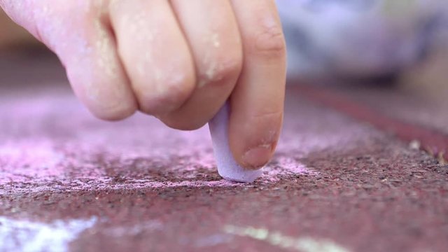 Hand of little girl drawing with chalk on ground slow motion tracking shot