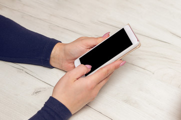 Female hands hold a smartphone over a wooden table