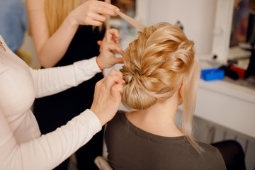 Fototapeta premium Hairdresser woman conducts training for pupil in salon, weaving braid hair, wedding styling.