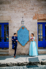 Obraz na płótnie Canvas elegant wedding couple gently hugging in sunlight in old courtyard in european street. luxury bride and groom embracing. romantic sensual moment. Woman in blue dress man in dark blue suite