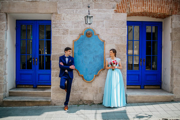 Fototapeta na wymiar elegant wedding couple gently hugging in sunlight in old courtyard in european street. luxury bride and groom embracing. romantic sensual moment. Woman in blue dress man in dark blue suite