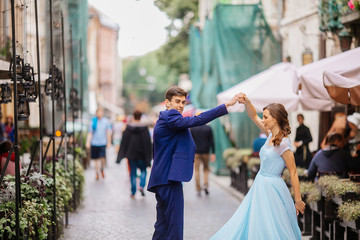 Portrait the groom in wedding suit and the bride in  dress walking back near old building, old house outside, outdoor. Newlyweds are walking along the streets. Kissing couple. Wedding walks. Dancing.