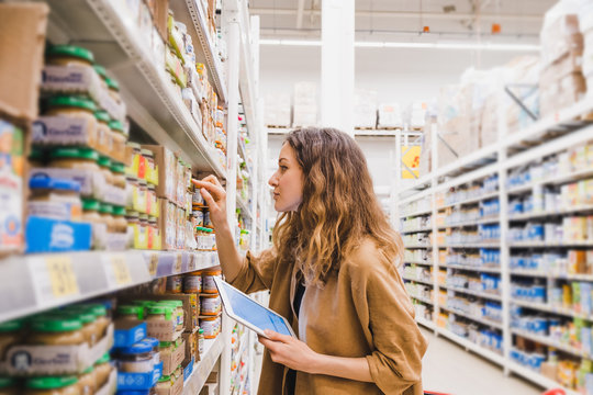 Young beautiful woman with a tablet picks baby food in a supermarket, the girl reads the composition of a product close-up