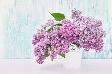 Lilac flowers bouquet in white vase on blue background. Holiday background, copy space. Spring background.