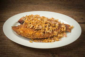 asia-asian food. thai food. fried nile tilapia river fish with garlic. on dish ceramic. on old wood background
