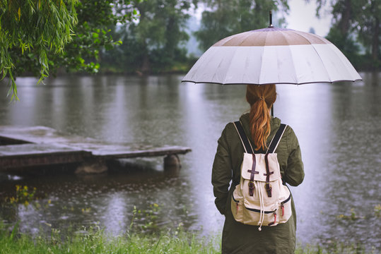woman with umbrella and backpack standing in  rain at lake