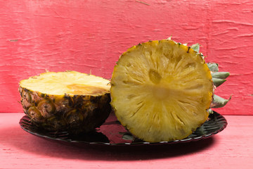 pineapple on dish half on pink wood.
