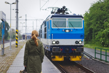 Traveler woman standing on railway station and waiting for a train 