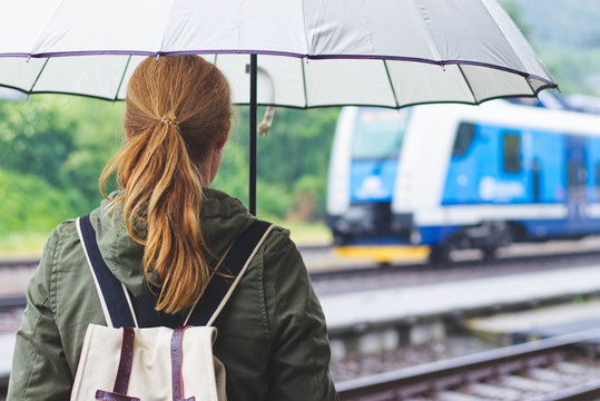 Woman with umbrella looking at the arriving train at the train station platform
